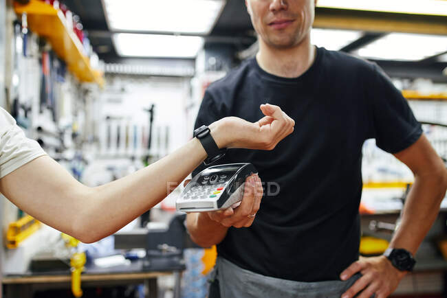 Weicher Fokus des männlichen Mechanikers mit Terminal, der kontaktlose Zahlungen von Erntekunden mit Smartwatch während der Arbeit in der Garage erhält — Stockfoto