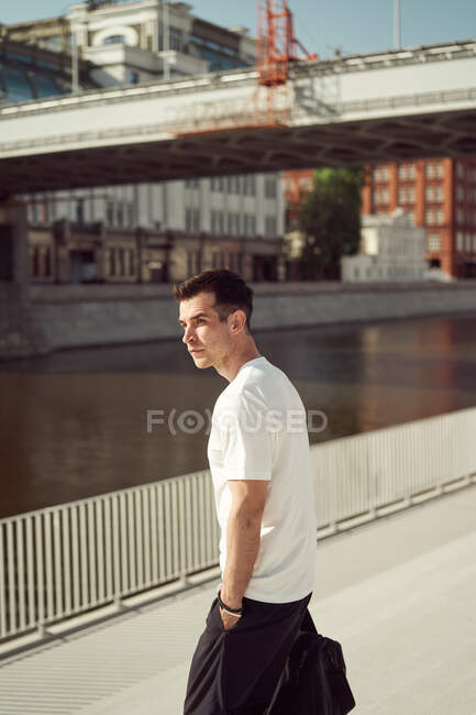 Atleta masculino com saco esportivo em pé em aterro na cidade no verão — Fotografia de Stock