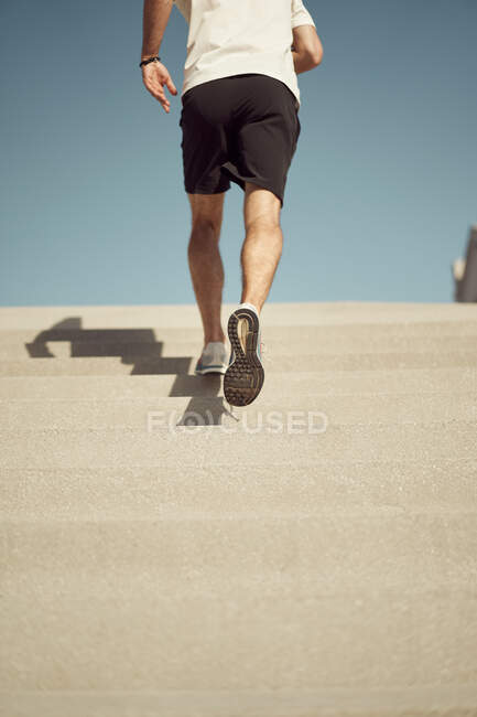 Back view of cropped unrecognizable athletic male running upstairs while training on sunny day in city in summer — Stock Photo