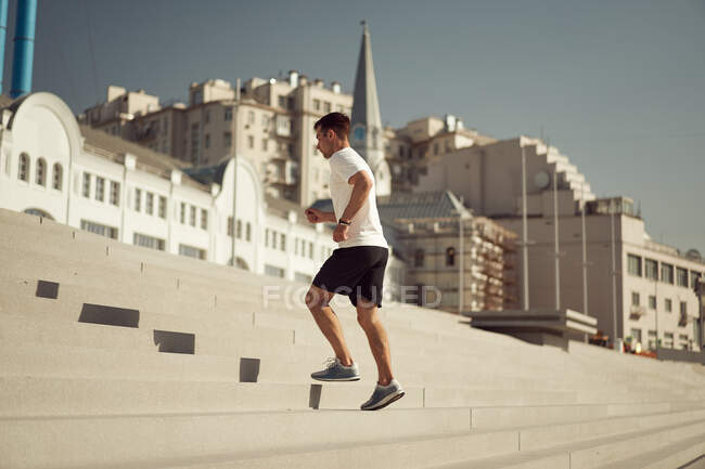 Seitenansicht des athletischen Mannes, der an einem sonnigen Tag in der Stadt im Sommer die Treppe hochläuft — Stockfoto