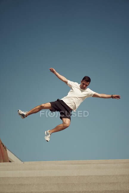 Нижче активного чоловіка стрибає високо і показує паркур трюк на блакитне небо влітку — стокове фото