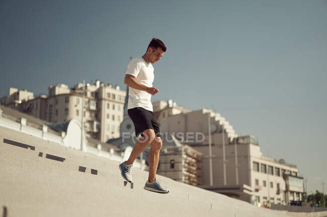 Vista laterale del maschio atletico che corre giù mentre si allena nella giornata di sole in città in estate — Foto stock