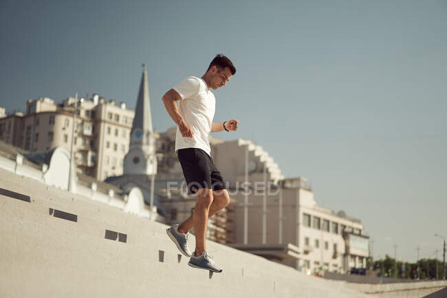 Вид сбоку спортивного мужчины, бегущего вниз во время тренировок в солнечный день в городе летом — стоковое фото