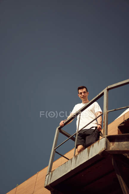 De baixo de atleta masculino positivo em activewear em pé na escada de metal perto do edifício e olhando para a câmera — Fotografia de Stock