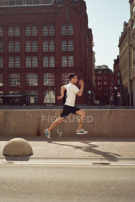 Seitenansicht eines starken männlichen Athleten, der im Sommer beim aktiven Training in der Stadt die Straße entlang springt — Stockfoto