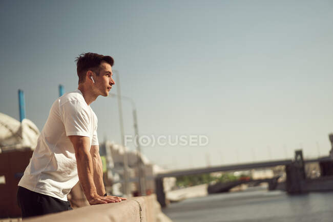 Seitenansicht eines männlichen Athleten in drahtlosen Kopfhörern, der während des Trainings im Sommer auf der Promenade in der Stadt Musik hört — Stockfoto