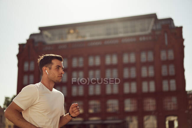 Seitenansicht eines starken männlichen Athleten, der im Sommer beim aktiven Training in der Stadt entlang der Straße läuft — Stockfoto