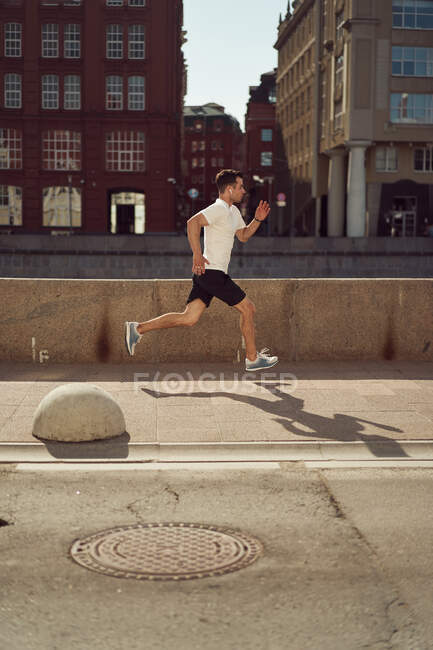 Side view of strong male athlete jumping along street during active workout in city in summer — Stock Photo