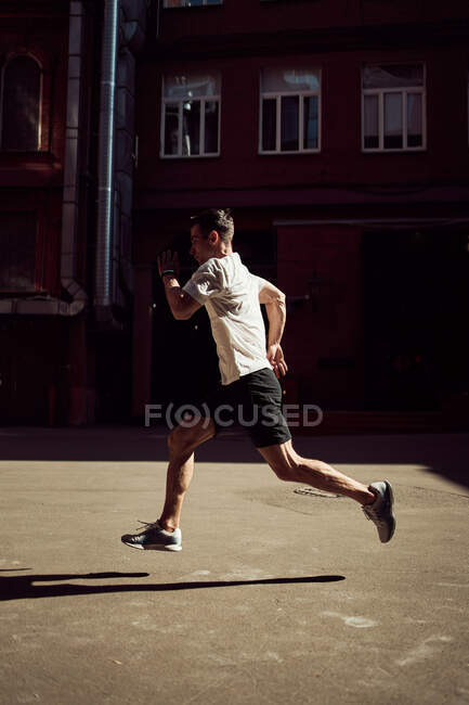 Side view of male running on street while training in city in summer — Stock Photo
