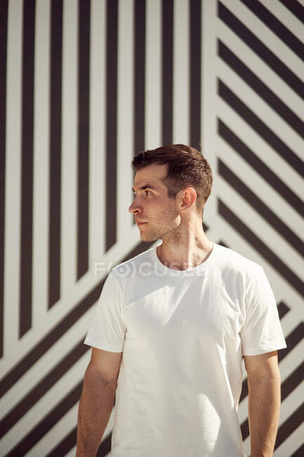 Serious sportsman in activewear standing on street in summer and looking away against stripe wall background — Stock Photo