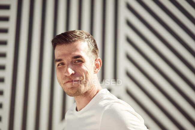 Happy smiling sportsman in activewear standing on street in summer and looking at camera against stripe wall background — Stock Photo