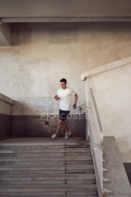 Подходящий бегун в спортивной одежде бегущий вниз по городу во время активных тренировок летом — стоковое фото