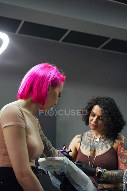 Мастер татуировок в перчатках, используя профессиональную татуировку во время рисования татуировки на руке женщины в современной студии татуировки — стоковое фото