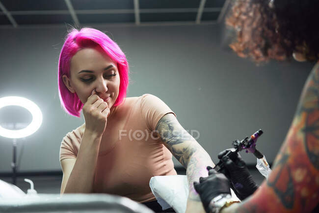Tatuaggio master in guanti utilizzando la macchina professionale del tatuaggio mentre dipingi il tatuaggio sul braccio della donna nel moderno studio del tatuaggio — Foto stock