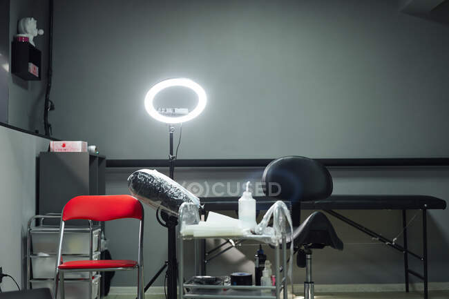 Interno del moderno salone del tatuaggio con sedie e tavolo con varie attrezzature accanto alla lampada ad anello e all'armadio — Foto stock