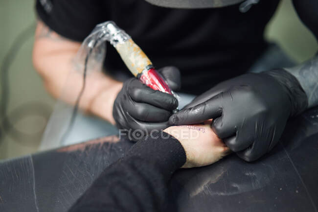 Konzentrierte männliche Tätowierer in Handschuhen machen Tätowierung auf der Hand des Kunden, während mit professionellen Tätowiermaschine in modernen Tätowierstudio — Stockfoto
