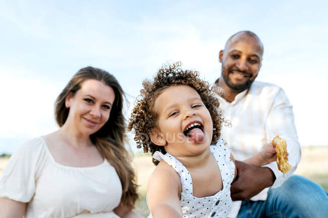 Felice famiglia multietnica con carina figlioletta godendo picnic estivo in natura — Foto stock