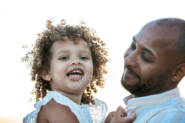 African American father holding cute curly haired African American daughter on background of sundown sky in nature looking at camera — Stock Photo