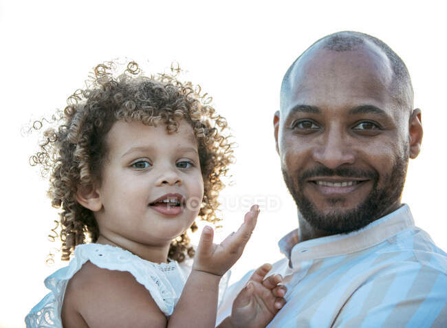 Afro-américain père tenant mignon frisé cheveux fille afro-américaine sur fond de coucher de soleil ciel dans la nature en regardant la caméra — Photo de stock