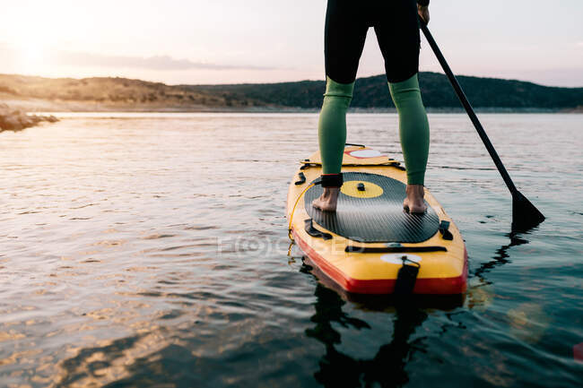 Обрізаний невпізнаваний анонімний чоловічий серфер, що плаває на дошці SUP на спокійному морі на заході сонця влітку — стокове фото