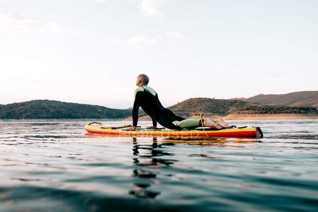 Side view of unrecognizable male surfer practicing yoga in bhujangasana pose on SUP board in sea at sunset — Stock Photo