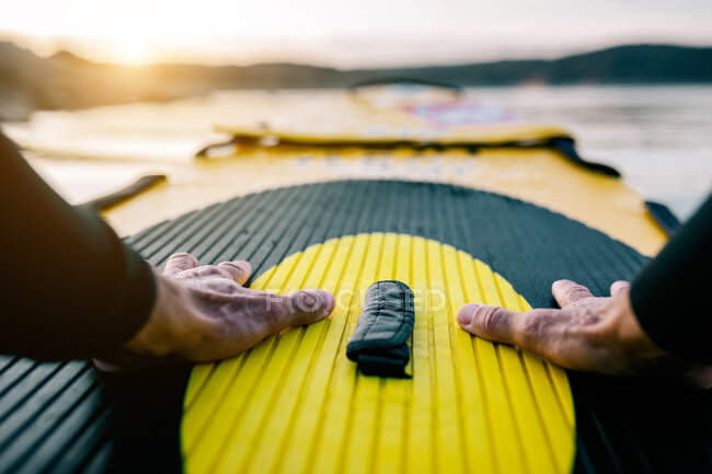 POV vista de las manos de cultivo de surfista masculino anónimo flotando en la tabla SUP en el mar al atardecer - foto de stock