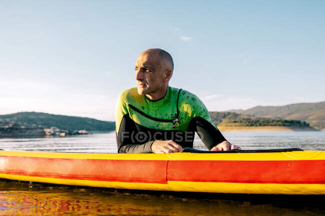 Male in wetsuit lying on paddle board and swimming on lake surface while practicing water sport in summer day — Stock Photo