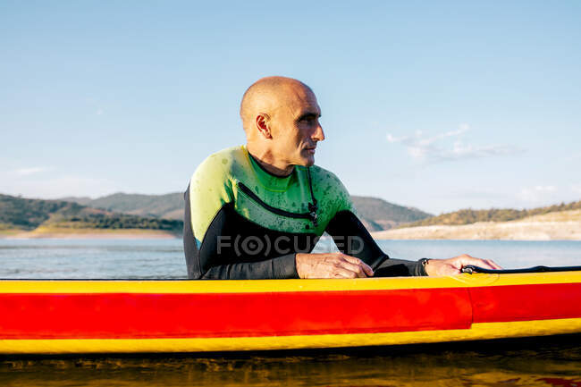 Männchen im Neoprenanzug liegt auf dem Paddelbrett und schwimmt auf der Oberfläche des Sees, während sie im Sommer Wassersport treiben — Stockfoto