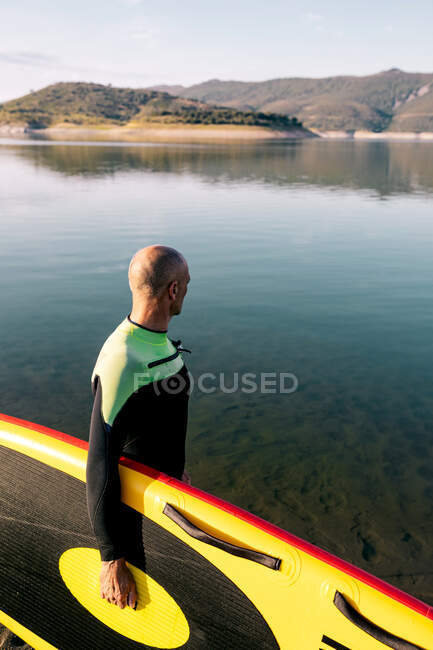 Vue latérale d'un surfeur mâle non reconnaissable en combinaison debout avec planche à SUP jaune et pagaie dans l'eau de mer — Photo de stock