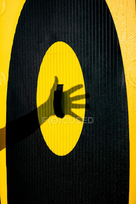 Unrecognizable person keeping hand on bright yellow and black paddle board against sunlight — Stock Photo