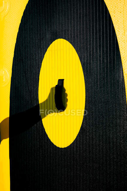 Unrecognizable person keeping hand on bright yellow and black paddle board against sunlight — Stock Photo