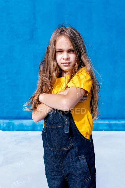 Adolescent confiant debout avec les bras croisés sur fond bleu et regardant la caméra — Photo de stock