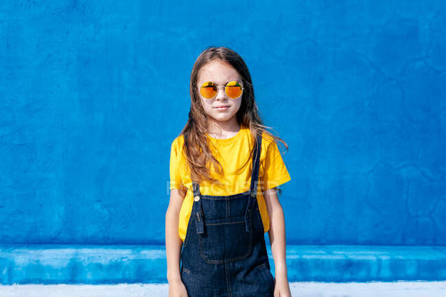 Fidato adolescente in piedi con occhiali da sole alla moda sfondo blu e guardando la fotocamera — Foto stock