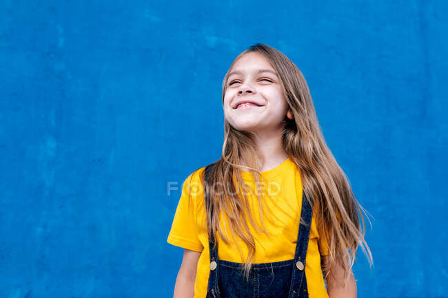Entzückter verträumter Teenager steht vor blauem Hintergrund und schaut weg — Stockfoto