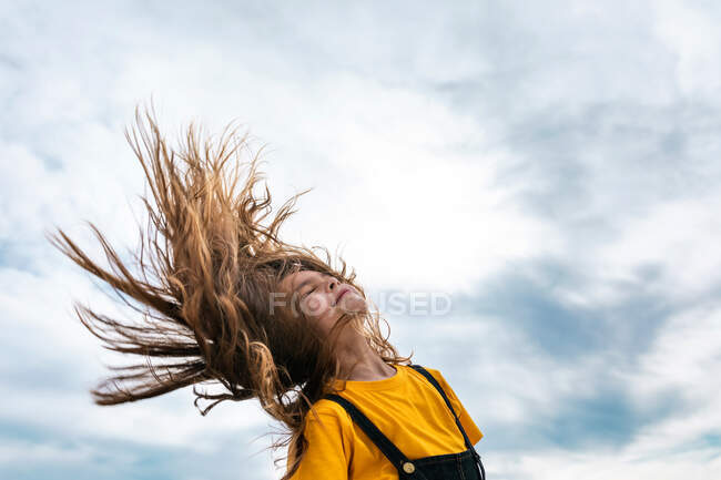 Vista laterale dal basso di tranquilla adolescente gettando i capelli lunghi sullo sfondo del cielo nuvoloso in estate — Foto stock