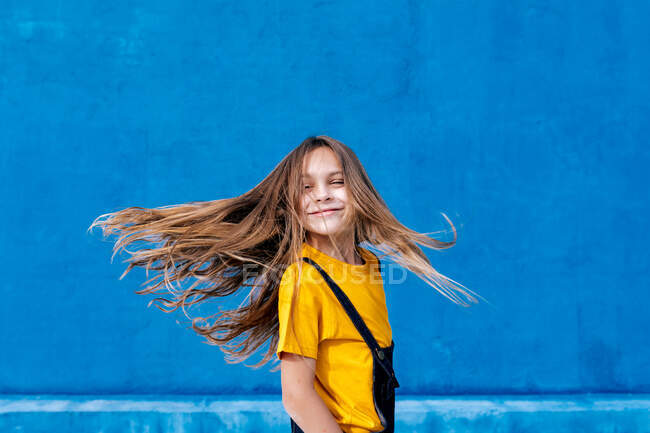 Entzückter verträumter Teenager mit langem fliegendem Haar, der vor blauem Hintergrund wegschaut — Stockfoto