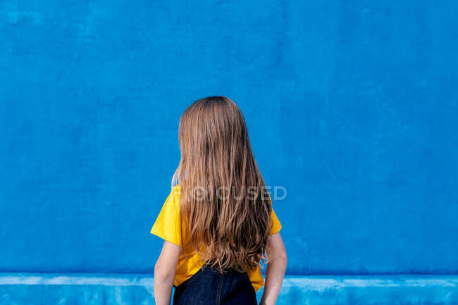 Anonymous cool teenager with long hair standing on blue background — Stock Photo