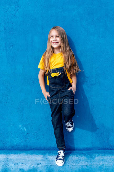 Веселий підліток-гіпстер з купою жовтих квітів в кишені деніма в цілому схилившись на синій стіні і дивлячись геть — стокове фото