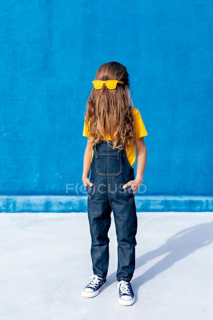 Adolescente legal anônimo usando óculos de sol amarelos no rosto de cobertura de cabelo longo no fundo azul — Fotografia de Stock