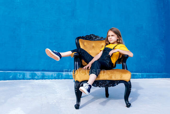 Thoughtful teen hipster sitting on chair on blue background looking away — Stock Photo