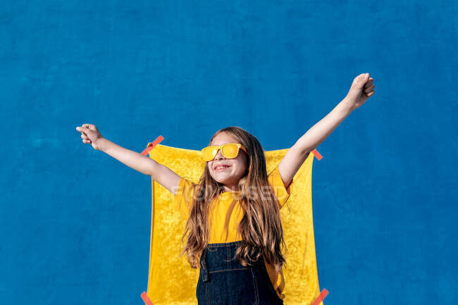 Teenie-Hipster mit Sonnenbrille und langen Haaren feiern Sieg mit erhobenen Armen auf gelb-blauem Hintergrund — Stockfoto