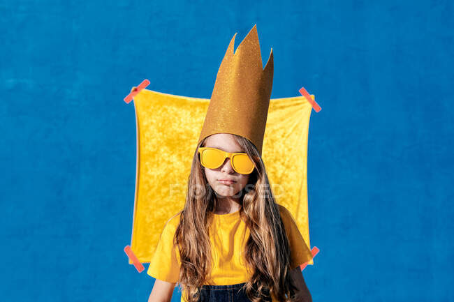 Крутой хипстер-подросток в золотой короне и солнечных очках, стоящий, глядя в камеру на двух цветном фоне — стоковое фото
