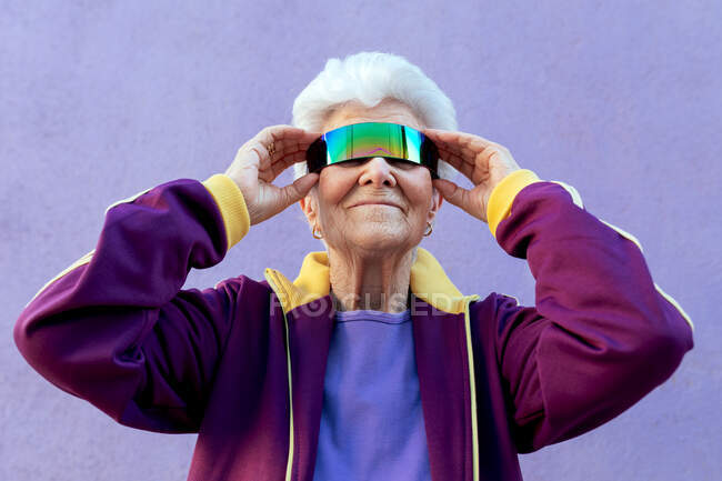 Cheerful elderly female athlete with gray hair in sportswear and blindfold on violet background — Stock Photo