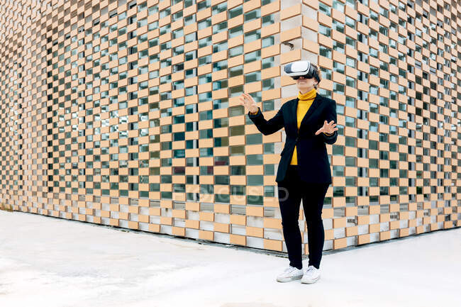 Усміхнена жінка в куртці і черепашці використовує окуляри VR біля будівельних вікон в денний час — стокове фото
