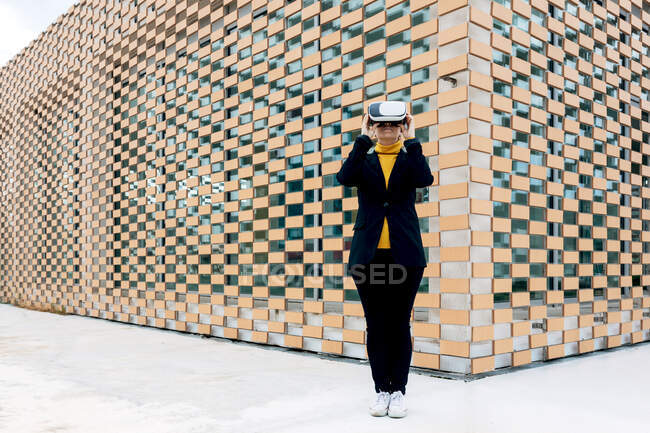 Женщина в куртке и водолазке с защитными очками возле окон здания при дневном свете — стоковое фото