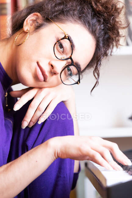 Vista lateral de una joven hispana tocando el piano eléctrico mientras practica habilidades musicales en casa - foto de stock