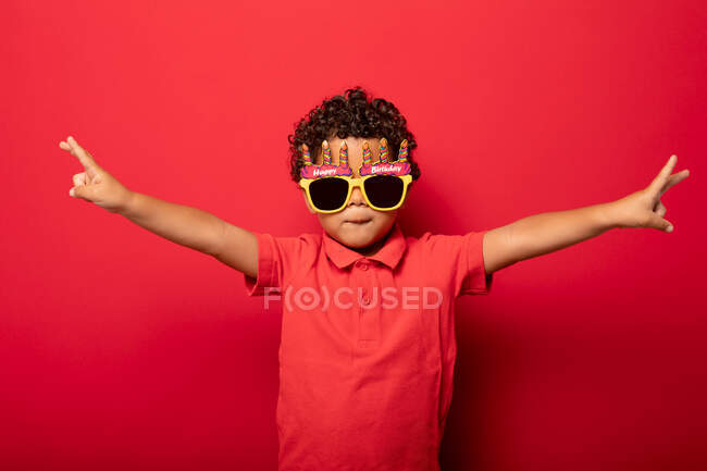 Criança legal vestindo brilhantes óculos de sol Feliz Aniversário mostrando gesto de paz no fundo vermelho em estúdio — Fotografia de Stock