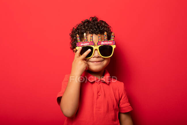 Прохолодна дитина в яскравих сонцезахисних окулярах Happy Birthday на червоному тлі в студії — стокове фото