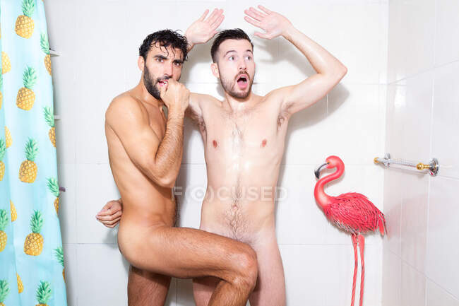 Веселі грайливі голі багатоетнічні гомосексуальні хлопці розважаються, приймаючи душ разом у ванній кімнаті з рожевим фламінго — стокове фото
