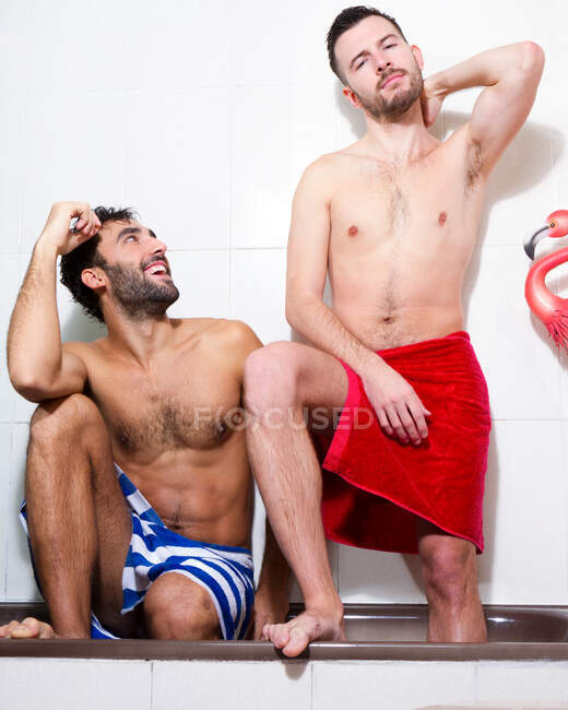 Confident adult multiracial gay pärchen mit nackt torsos und handtücher looking at camera während having bath time together im badezimmer — Stockfoto